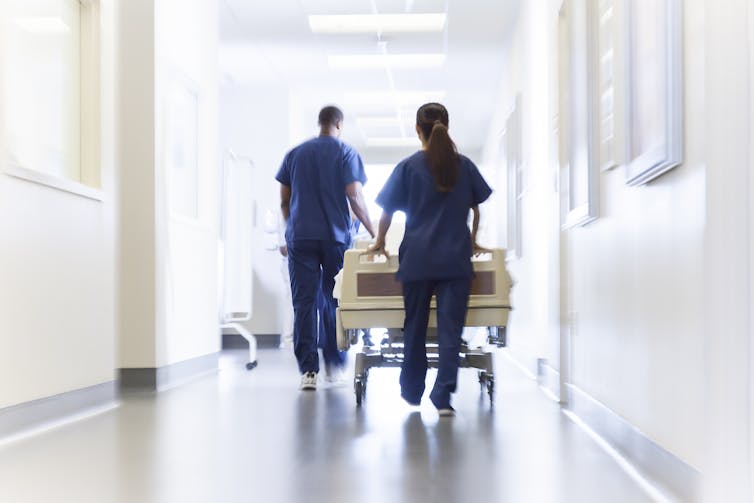 Two hospital staff pushing a bed through a hospital corridor.