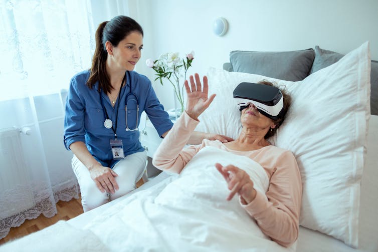 An older woman in bed uses a VR gaming headset.