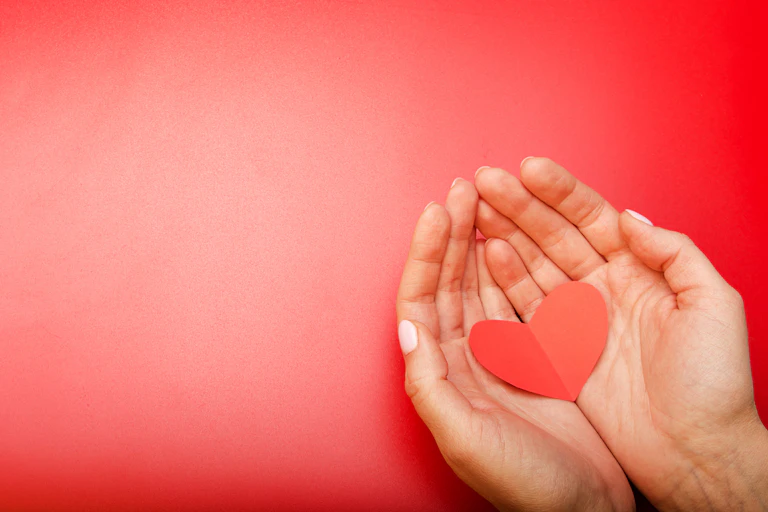 Two hands holding a red paper heart against a red background