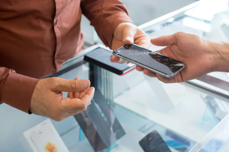 main qui donne un smartphone cassé dans une autre main