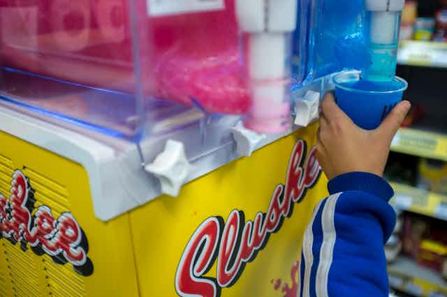 Child's hand reaching up to get a blue slushy from a dispenser