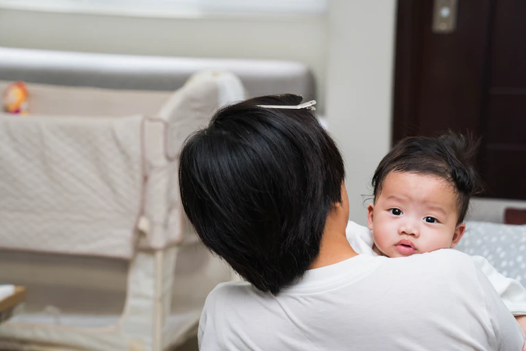 A person burps their baby on their shoulder.