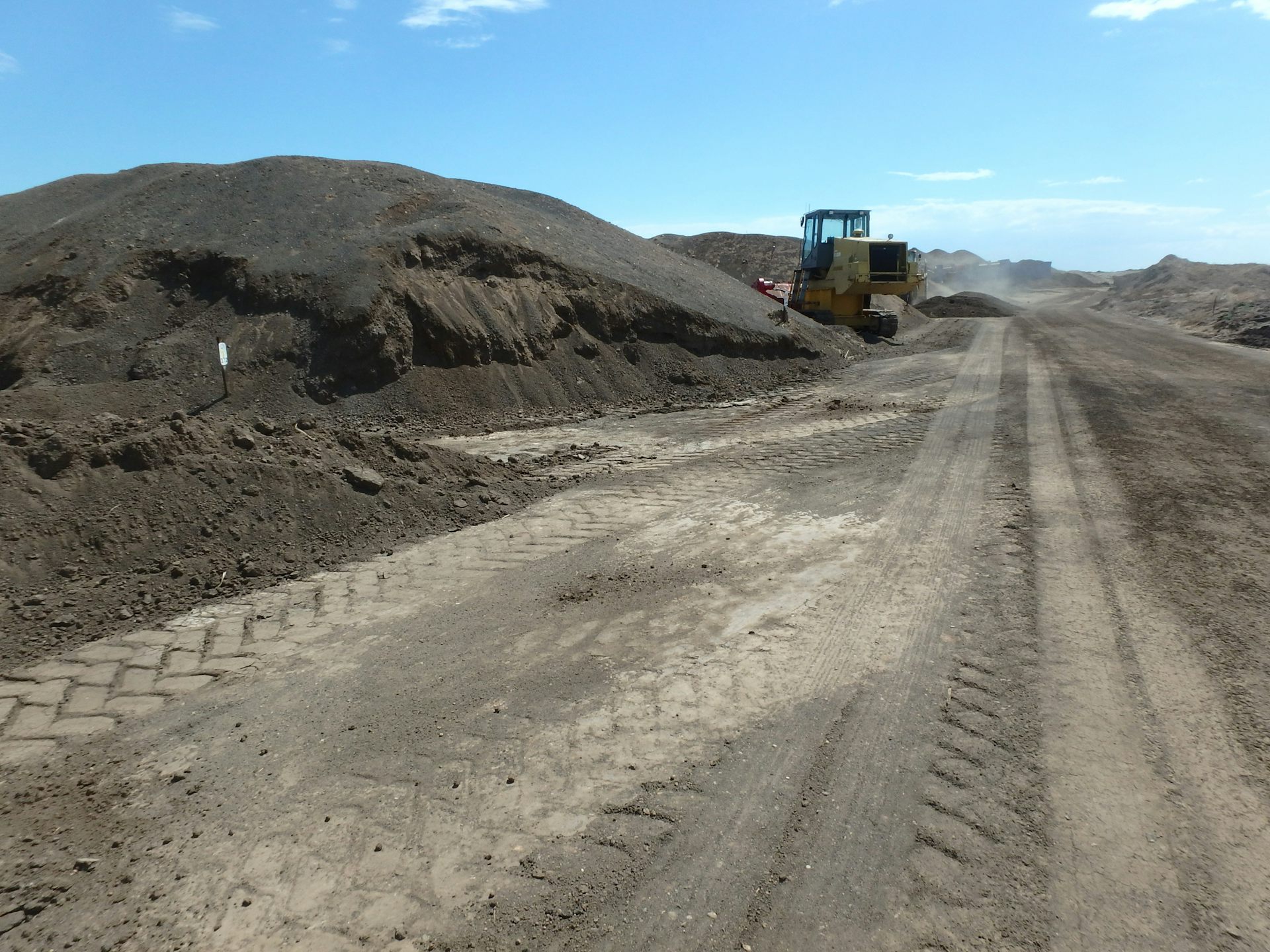 Stockpiles of biosolids from sludge lagoons with a tractor in the background
