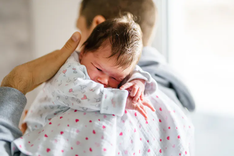 A man gently pats his newborn baby on the back.