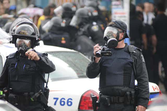 two police officers in riot gear, one holding a camcorder