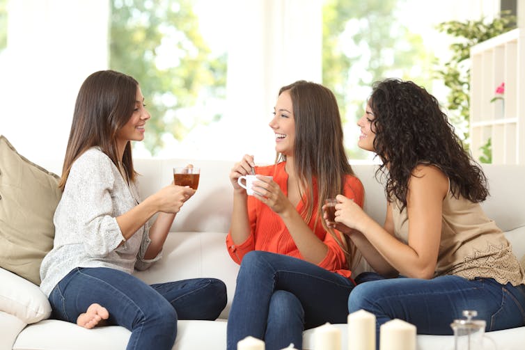 Three female friends sitting on a couch as they have a cup of coffee