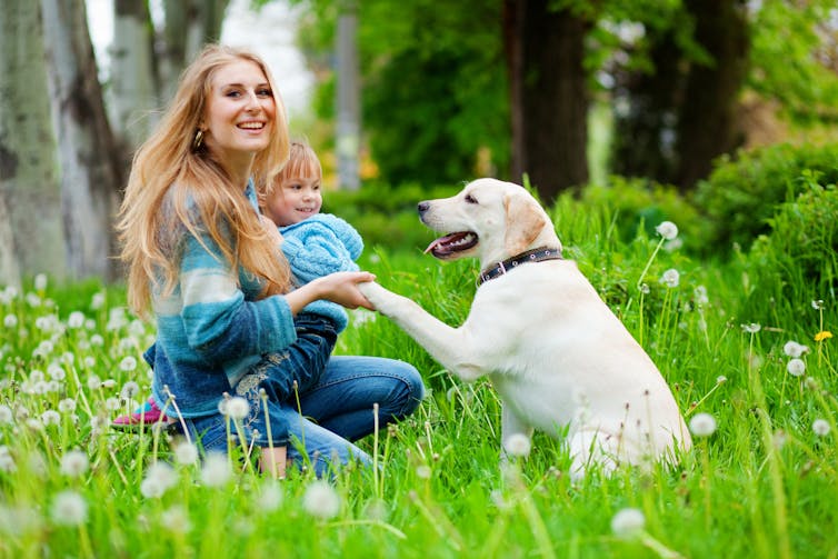 Woman holding a child and shaking a dog's paw