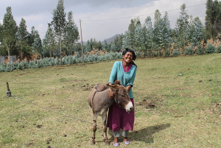 A rural woman standing next to her donkey in a field.