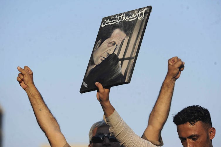 A supporter holding up a placard depicting Imran Khan on a clear, sunny day.