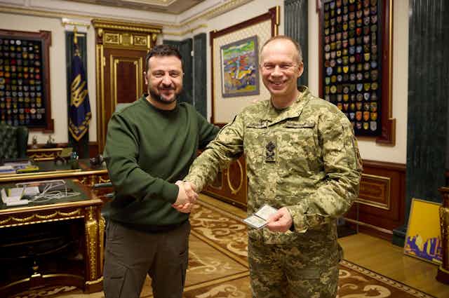 Ukrainian president Volodymyr Zelensky,  smiles as he shakes hands with his new commander-in-chief Oleksandr Syrskyi.