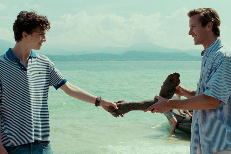 A young man and an older man looking at each other with a seascape in the background.