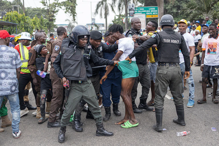 Men in police uniform arresting a young man on the street.