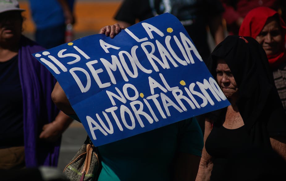A protester holds up a blue banner wit hthe words 'Iisi a la democracia no al authoritarismo' on it.