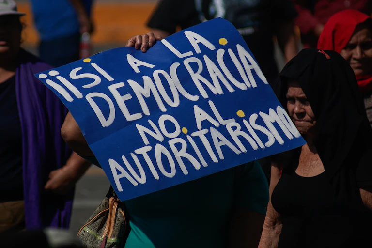 A protester holds up a blue banner wit hthe words 'Iisi a la democracia no al authoritarismo' on it.