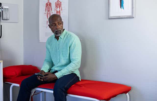 A black male patient with a salt-and-pepper beard sitting on examination table at a doctor's office