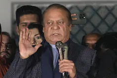 A balding man glares and gestures as he speaks into a microphone.