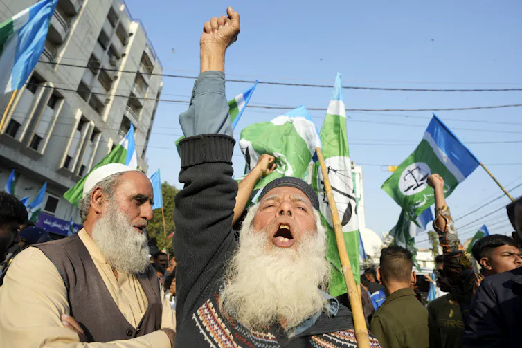A man with a long grey beard shouts a slogan with his arm raised.