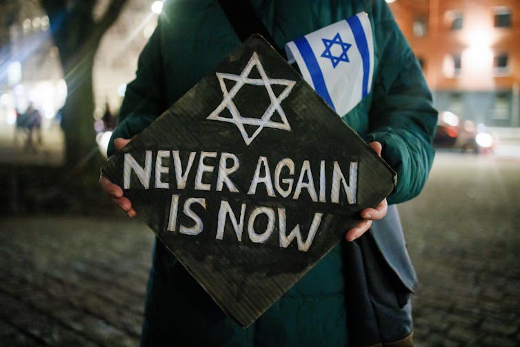 A placard reading Never Again Is Now with the Israeli flag.