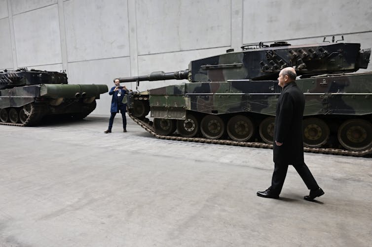 A man walks past a military tank.