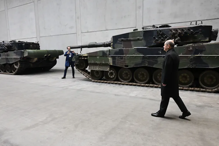 A man walks past a military tank.