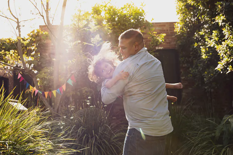 An Aboriginal man plays with his young daughter in the backyard.