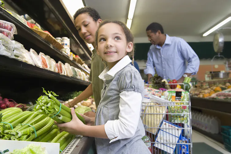 Girl picks up celery while shopping with her brother and dad