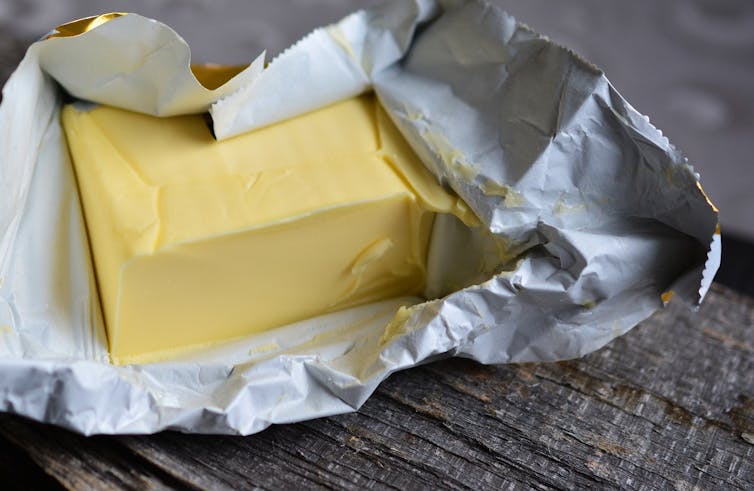 A block of yellow butter in an open silver foil wrapper