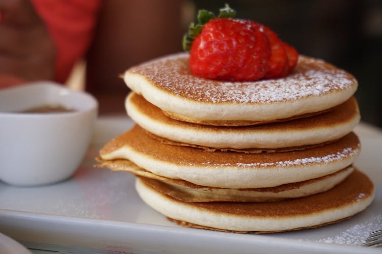 A stack of fluffy pancakes dusted with sugar with a strawberry on top