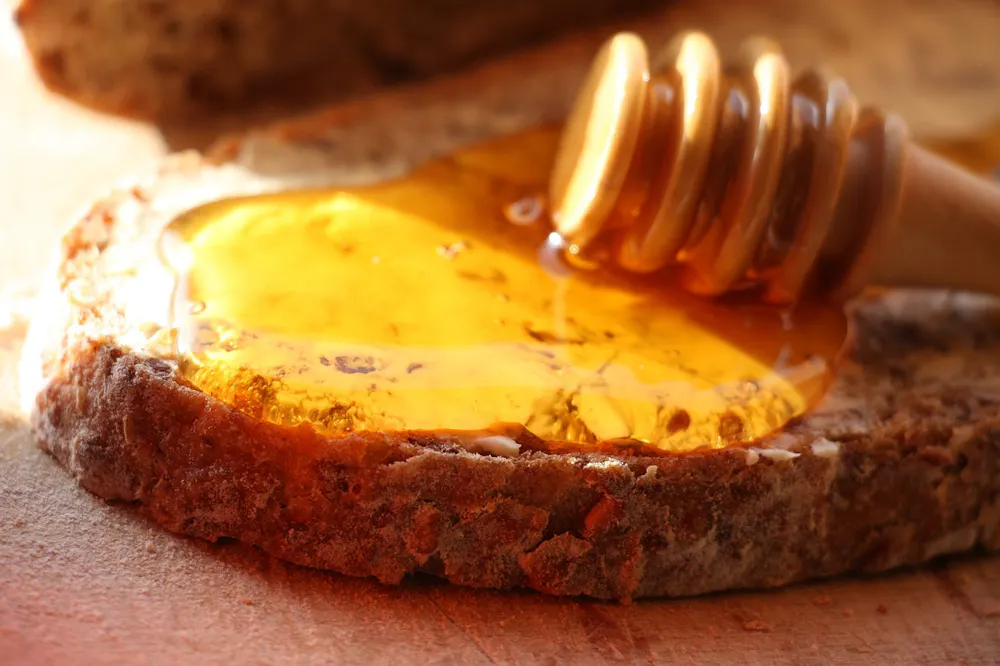 Primer plano de una rebanada de pan con miel dorada acumulada en la superficie