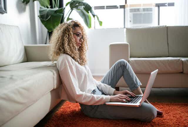 Young woman sits on her loungeroom floor, on her laptop