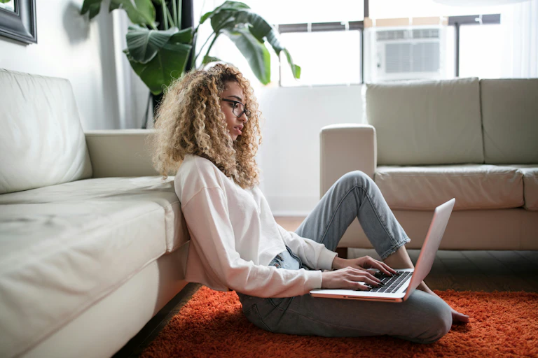 Young woman sits on her loungeroom floor, on her laptop