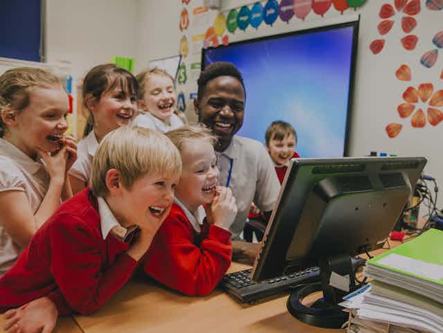 Teacher and pupils laughing at computer