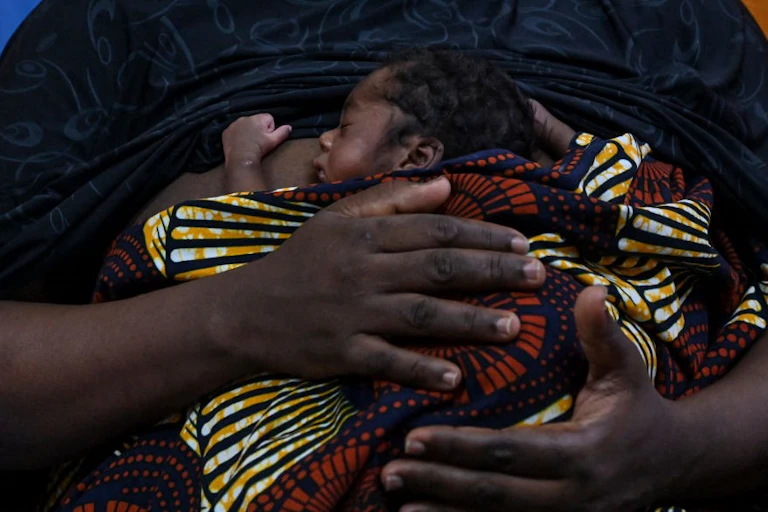 A very small infant wrapped in a cloth, held against a woman's torso.