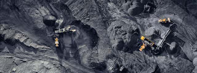 Aerial shot looking down on black coal pits being mined, five yellow and black machines