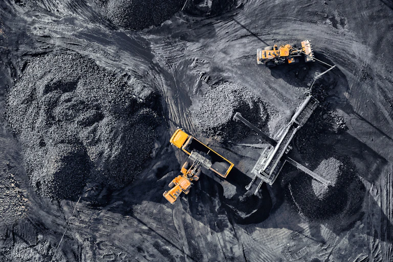 Aerial shot looking down on black coal pits being mined, five yellow and black machines