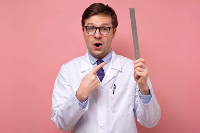 Man in a lab coat holding up a ruler and pointing to it