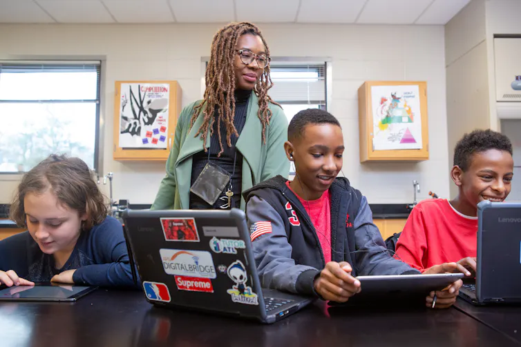 An adult seen behind children at computers.