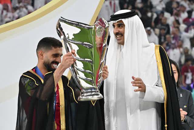 L'émir du Qatar et un joueur couvert de la cape traditionnelle sourient en brandissant la coupe d'Asie.