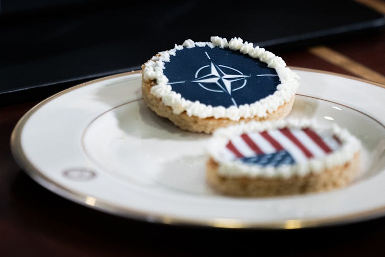 Two cookies are seen on a plate - one has frosting designed like the American flag, and the other is blue with a white compass on it.