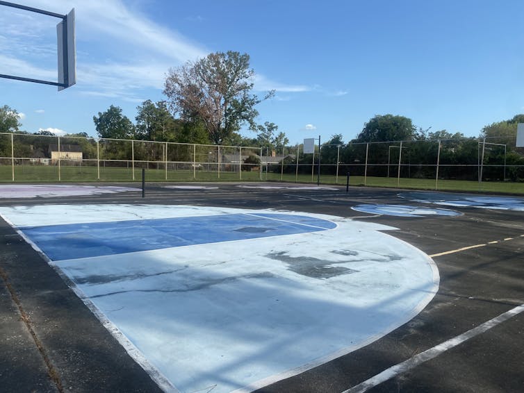 Cement surface surrounded by a fence with grass beyond. There's no playground equipment..