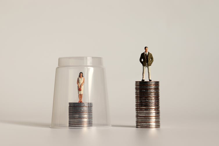 A figure of a woman standing on a stack of coins with a plastic cup placed over it. Beside it is a figure of a man standing on a taller stack of coins.