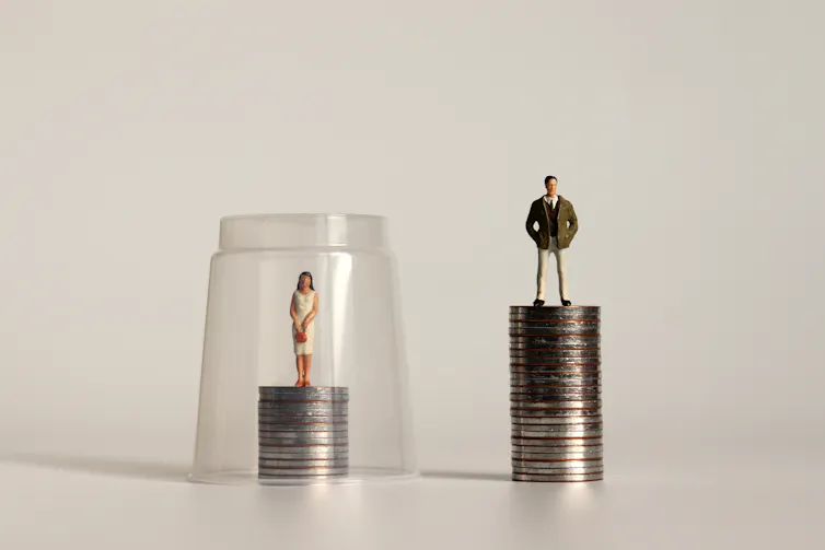 A figure of a woman standing on a stack of coins with a plastic cup placed over it. Beside it is a figure of a man standing on a taller stack of coins.
