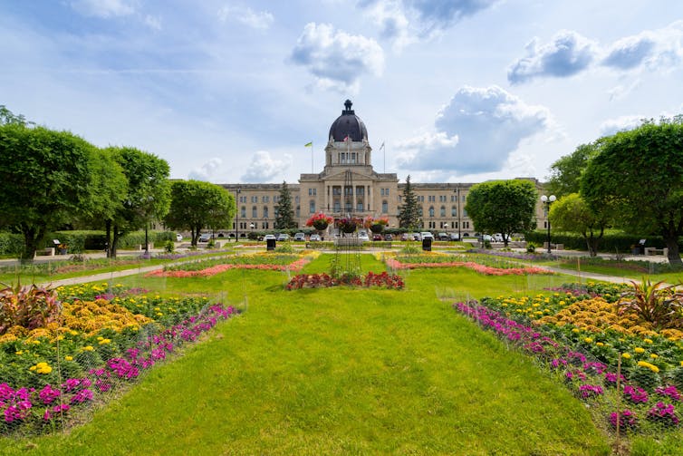 A large building stands in the background with a field and flower beds in the foregound.