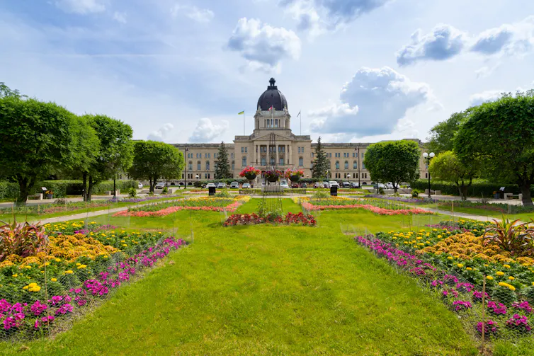 A large building stands in the background with a field and flower beds in the foregound.
