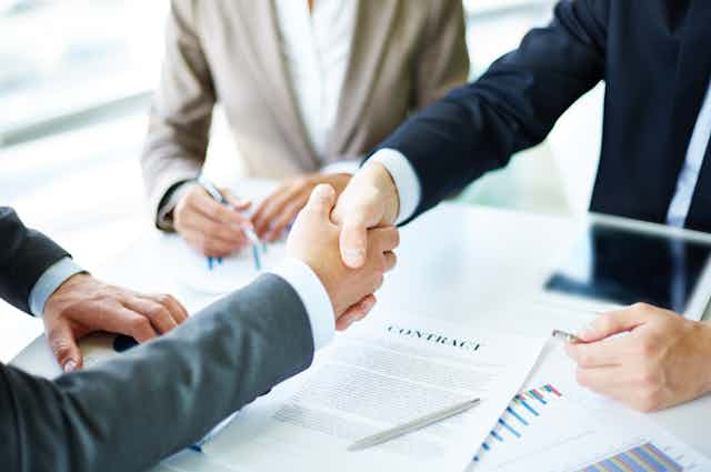 The arms of two men shaking hands over a contract on a table