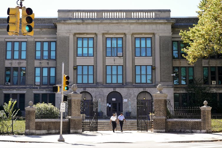 Three-story school building with police officers out front and traffic lights in the foreground