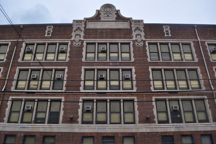 Front of a four-story brick school building with tall windows, some with air-conditioners