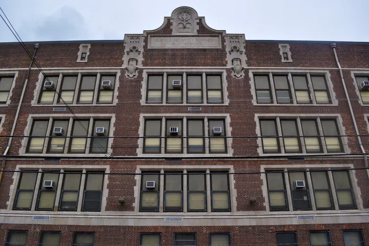 Front of a four-story brick school building with tall windows, some with air-conditioners