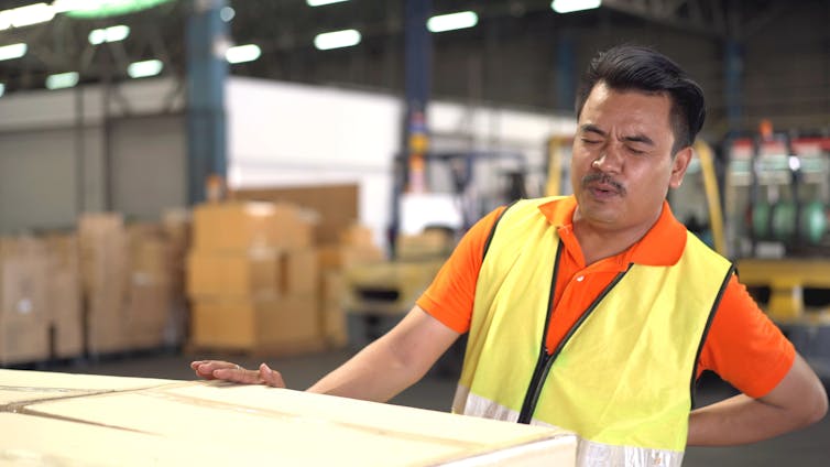 Factory worker deep-breathes with a sore back