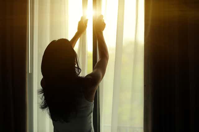 A woman closing the window at home.
